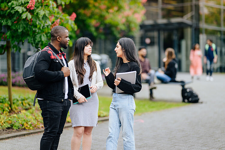Three people in conversation outside on the campus of Paderborn University.